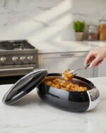 Modern sleek black insulated thermal hotpot casserole with metallic chrome accents on a kitchen counter with fresh hotpot ingredients