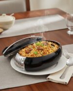Modern sleek black insulated thermal hotpot casserole with metallic chrome accents on a kitchen counter with fresh hotpot ingredients