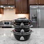 Stacked 3-piece black insulated hot pot set with chrome silver accents on a marble kitchen countertop.