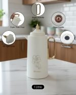 A professional display of three 1-liter Feenik vacuum thermoses in Black, White, and Coffee colors. Each flask features a gold-accented handle, a decorative gold floral print, and a push-to-pour lid, set against a clean kitchen background.