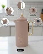 A professional display of three 1-liter Feenik vacuum thermoses in Black, White, and Coffee colors. Each flask features a gold-accented handle, a decorative gold floral print, and a push-to-pour lid, set against a clean kitchen background.