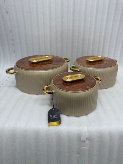 A professional studio shot of a set of three graduated-size insulated hotpots with gold handles, featuring a ribbed cream or grey body and decorative marble or wood-patterned lids, displayed on a kitchen countertop.