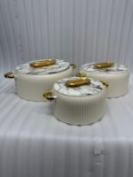 A professional studio shot of a set of three graduated-size insulated hotpots with gold handles, featuring a ribbed cream or grey body and decorative marble or wood-patterned lids, displayed on a kitchen countertop.