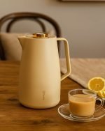 Feenik 2 liter thermal carafe vacuum flask displayed in Coffee, Grey, and White colors, featuring infographics highlighting the glass inside, airtight cap, sleek handle, push-button pouring, and sturdy plastic base.