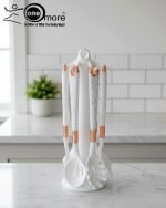 Luxury white marble-look cooking utensil set with rotating holder and rose gold accents. Includes spatula, spoon, and pasta server. Ideal kitchen decor centerpiece.