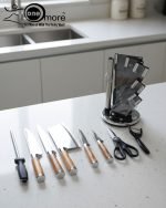 One More luxury 11-piece knife set in rotating stainless steel and clear acrylic block. Features black and gold accented handles, perfect as a modern kitchen centerpiece.