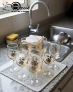 Elegant 7-piece glass water set by One More featuring one amber glass pitcher and six matching goblets, all decorated with a black and gold tulip design.