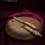 Gold-plated cake knife and server set with ornate handles, shown cutting a white birthday cake, a chocolate wedding cake slice, and displayed on a wooden board with a velvet BG. Elegant serving utensils.