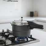 One More non-stick pressure cooker used as a steamer for three seasoned chicken drumsticks wrapped in foil on a metal rack.