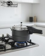 One More non-stick pressure cooker used as a steamer for three seasoned chicken drumsticks wrapped in foil on a metal rack.