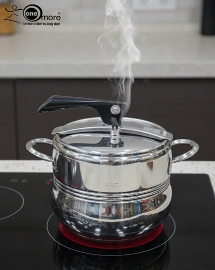 One More stainless steel pressure cooker releasing steam on an induction or ceramic electric cooktop.