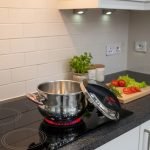 Top-down view of the O.M.S. Callacook 5-Litre Turkish pressure cooker lid. The lid features a sleek stainless steel and black plastic housing with two prominent red push buttons for the unique, easy-to-use locking and unlocking mechanism. A separate red lever near the edge controls the advanced pressure valve, highlighting the high-quality, modern design and superior safety features of this premium, imported Turkish cooker.