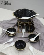 A complete 15-piece ceramic soup set displayed in a kitchen setting, featuring one large scalloped serving bowl, six small individual soup bowls, a golden metal storage stand, and seven white serving spoons. The set is available in six colors: black, dark gray-blue, navy blue, emerald green, beige/nude, and light mint green, all highlighted with an elegant gold rim.