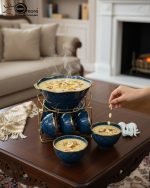 A complete 15-piece ceramic soup set displayed in a kitchen setting, featuring one large scalloped serving bowl, six small individual soup bowls, a golden metal storage stand, and seven white serving spoons. The set is available in six colors: black, dark gray-blue, navy blue, emerald green, beige/nude, and light mint green, all highlighted with an elegant gold rim.