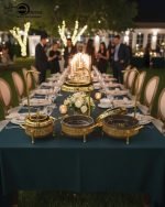 A collection of luxurious gold and deep brown Royal Buffet Server Chafing Dishes, available in 1.5, 2.2, and 3.2-liter sizes. The dishes feature intricate lattice detailing, clear-top lids, and elegant gold stands with hooks for convenient lid placement. The images show the servers beautifully displayed on formal dining and outdoor buffet tables, holding hot dishes like Biryani and curry, emphasizing their elegant design and food-warming capability for weddings and upscale events.