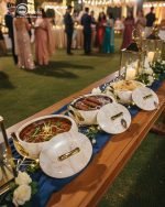 A set of three stacked white marble-patterned insulated casserole dishes (hot pots) with striking gold-tone handles and lids, displayed on a formal dining table.
