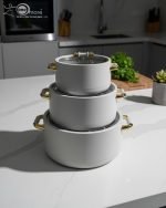 A stacked set of three premium insulated hot pots (1L, 2L, 3.5L) in a crisp white color with decorative gold-toned handles, shown on a marble kitchen countertop. The set features clear acrylic lids and is marketed for keeping food warm.