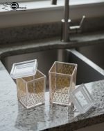 Clear acrylic storage jars with a subtle geometric pattern, shown holding snacks on a wooden table in a living room setting. Set of two sizes.