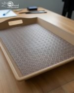 Set of three nesting fiber serving trays with non-slip textured surfaces and cut-out handles, displayed on a wooden dining table. The available colors are black, dark brown, grey, off-white, and rust-brown.