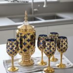 Luxury gold drink dispenser and goblet set with geometric pattern; available in two colors: royal blue/gold and emerald green/gold; featured on a modern kitchen counter.