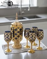 Luxury gold drink dispenser and goblet set with geometric pattern; available in two colors: royal blue/gold and emerald green/gold; featured on a modern kitchen counter.