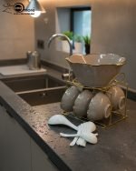 A complete 15-piece ceramic soup set displayed in a kitchen setting, featuring one large scalloped serving bowl, six small individual soup bowls, a golden metal storage stand, and seven white serving spoons. The set is available in six colors: black, dark gray-blue, navy blue, emerald green, beige/nude, and light mint green, all highlighted with an elegant gold rim.