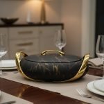 A set of three stacked white marble-patterned insulated casserole dishes (hot pots) with striking gold-tone handles and lids, displayed on a formal dining table.