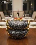 A set of three stacked white marble-patterned insulated casserole dishes (hot pots) with striking gold-tone handles and lids, displayed on a formal dining table.