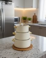 A stacked set of three premium insulated hot pots (1L, 2L, 3.5L) in a crisp white color with decorative gold-toned handles, shown on a marble kitchen countertop. The set features clear acrylic lids and is marketed for keeping food warm.