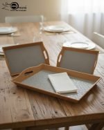 Set of three nesting fiber serving trays with non-slip textured surfaces and cut-out handles, displayed on a wooden dining table. The available colors are black, dark brown, grey, off-white, and rust-brown.