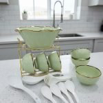 A complete 15-piece ceramic soup set displayed in a kitchen setting, featuring one large scalloped serving bowl, six small individual soup bowls, a golden metal storage stand, and seven white serving spoons. The set is available in six colors: black, dark gray-blue, navy blue, emerald green, beige/nude, and light mint green, all highlighted with an elegant gold rim.