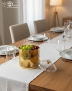 Close-up of a luxury two-tier gold fluted acrylic dish filled with green grapes and cherries, placed on a white table runner on a wooden dining table.