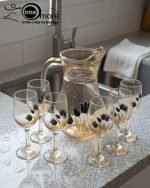 Elegant 7-piece glass water set by One More featuring one amber glass pitcher and six matching goblets, all decorated with a black and gold tulip design.