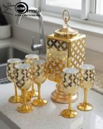 Fancy gold-tone beverage dispenser set with six matching stemmed goblets. The dispenser and glasses have a repeating geometric lattice pattern available in white and gold, blue and gold, or red and gold.