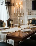 Fancy gold-tone beverage dispenser set with six matching stemmed goblets. The dispenser and glasses have a clear body overlaid with a delicate, scrolling gold floral pattern, and the goblets have solid gold bases.