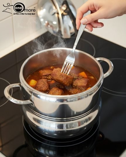 One More stainless steel pressure cooker releasing steam on an induction or ceramic electric cooktop.