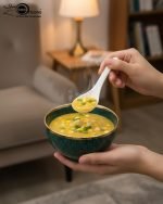 A complete 15-piece ceramic soup set displayed in a kitchen setting, featuring one large scalloped serving bowl, six small individual soup bowls, a golden metal storage stand, and seven white serving spoons. The set is available in six colors: black, dark gray-blue, navy blue, emerald green, beige/nude, and light mint green, all highlighted with an elegant gold rim.