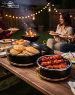 Set of three black insulated hot pot casseroles with gold trim and loop handles, sitting on a wooden dining table with a formal place setting.