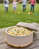 Set of three black insulated hot pot casseroles with gold trim and loop handles, sitting on a wooden dining table with a formal place setting.