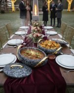 A set of three stacked white marble-patterned insulated casserole dishes (hot pots) with striking gold-tone handles and lids, displayed on a formal dining table.