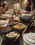 A set of three stacked white marble-patterned insulated casserole dishes (hot pots) with striking gold-tone handles and lids, displayed on a formal dining table.