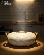 A set of three stacked white marble-patterned insulated casserole dishes (hot pots) with striking gold-tone handles and lids, displayed on a formal dining table.