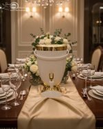 Insulated, stylish beverage dispenser (water cooler) with gold accents on base and spigot, shown in white, green, and chocolate/taupe colors, used for serving drinks on a dining table or kitchen counter.