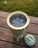Insulated, stylish beverage dispenser (water cooler) with gold accents on base and spigot, shown in white, green, and chocolate/taupe colors, used for serving drinks on a dining table or kitchen counter.