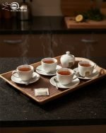 Set of three nesting fiber serving trays with non-slip textured surfaces and cut-out handles, displayed on a wooden dining table. The available colors are black, dark brown, grey, off-white, and rust-brown.