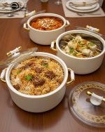 A stacked set of three premium insulated hot pots (1L, 2L, 3.5L) in a crisp white color with decorative gold-toned handles, shown on a marble kitchen countertop. The set features clear acrylic lids and is marketed for keeping food warm.