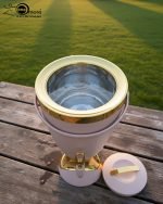 Insulated, stylish beverage dispenser (water cooler) with gold accents on base and spigot, shown in white, green, and chocolate/taupe colors, used for serving drinks on a dining table or kitchen counter.