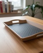 Set of three nesting fiber serving trays with non-slip textured surfaces and cut-out handles, displayed on a wooden dining table. The available colors are black, dark brown, grey, off-white, and rust-brown.
