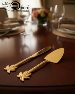 Luxurious golden cake knife and serving set with detailed palm leaf handles resting on a polished dark wood dining table, set for a formal dinner.