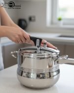 One More stainless steel pressure cooker releasing steam on an induction or ceramic electric cooktop.